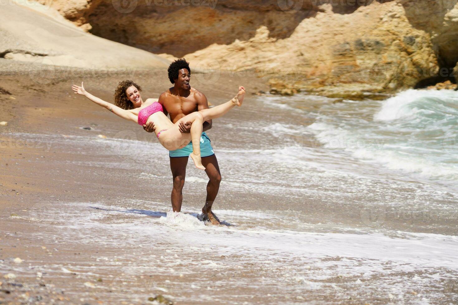 Young black man lifting up woman on beach photo
