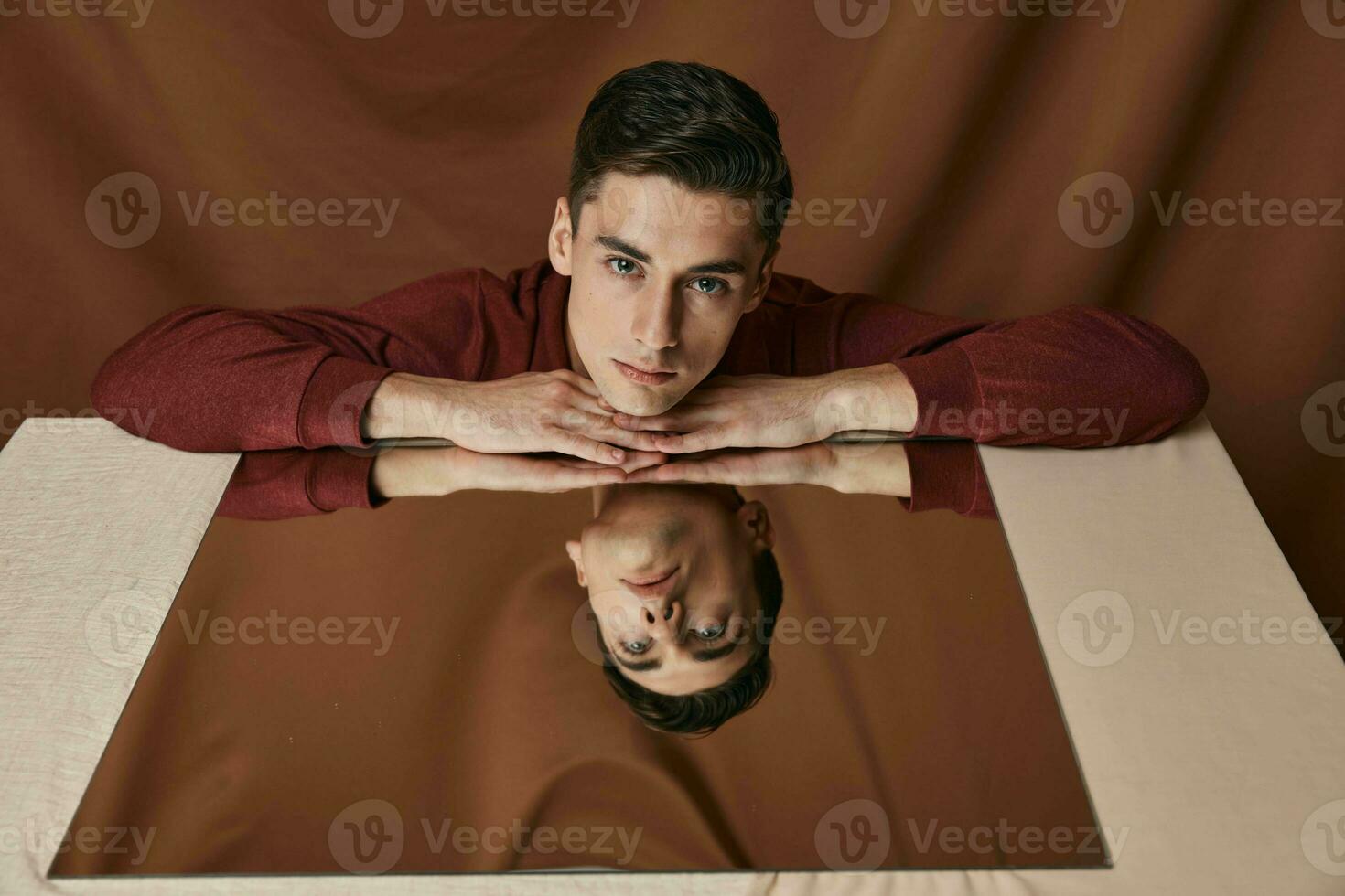 A man in a shirt put his hands on a mirror on the table and a brown pattern background photo