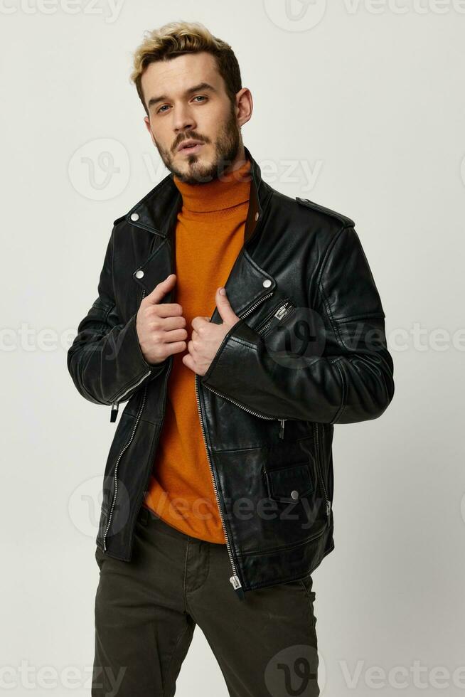 a man in an orange sweater straightens a leather jacket on a light background and fashionable trousers photo