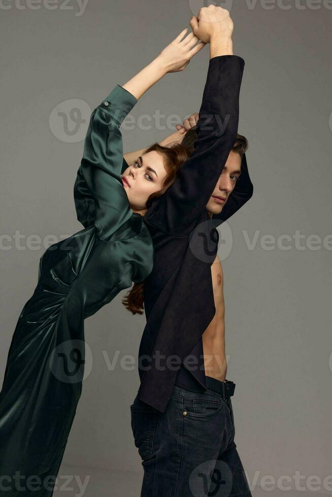 A woman in an evening dress and a man in a suit with raised hands on a gray background photo