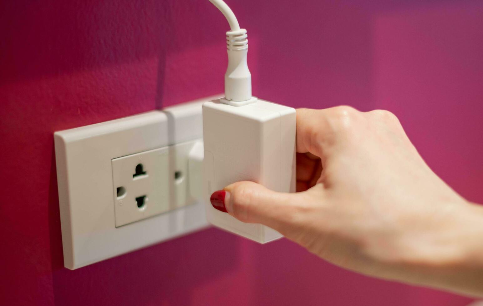 Hand is unplug the electric line off a white socket on the red wall. photo