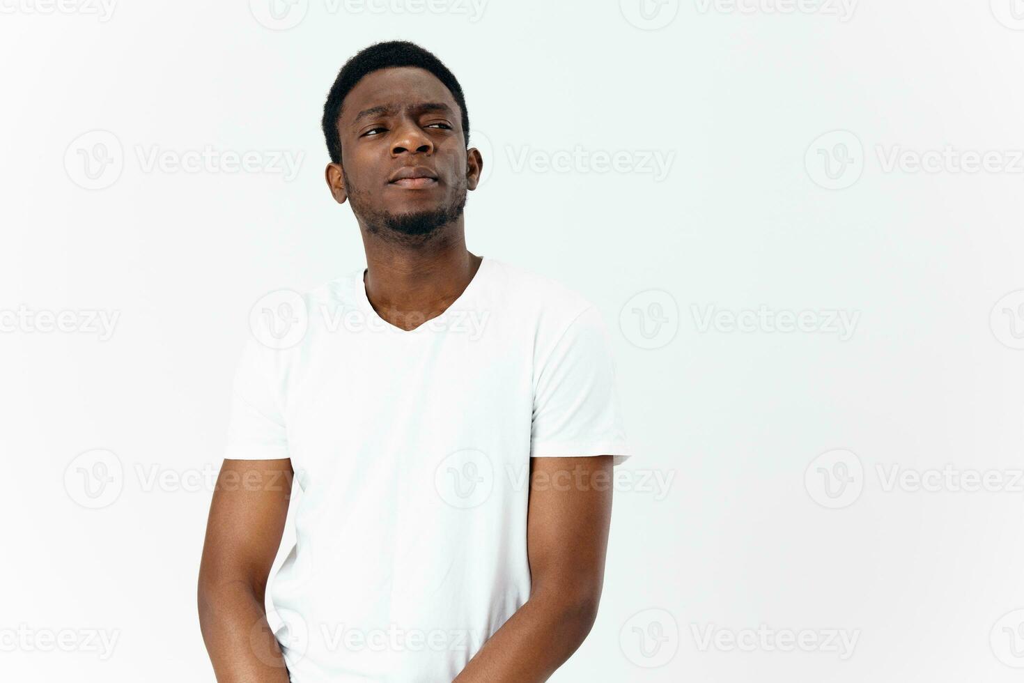 a pretty African guy in a white T-shirt looks to the side on a light background Copy Space photo