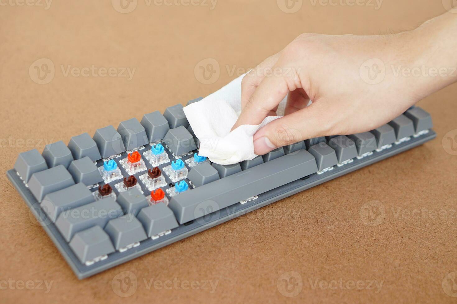 Closeup hand use tissue paper to clean wireless computer keyboard. Concept hygiene and disinfection on computer device that may have dust, germs, bacteria or virus on it photo