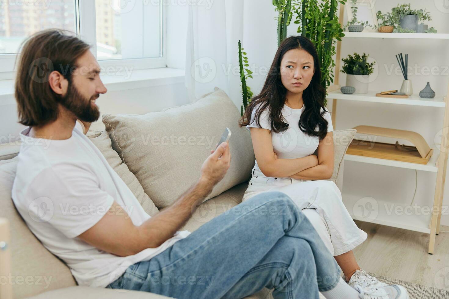 A man looks at the phone screen during an argument with his girlfriend. The angry and hurt woman looks in his direction and is sad. Family discord at home, phone addiction photo