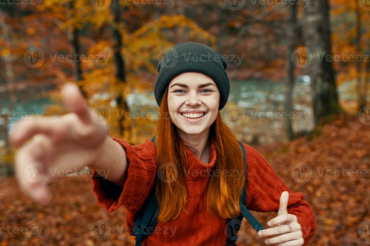 happy woman with a backpack travels in the park in autumn and gesticulate with the hands of the river in the background photo