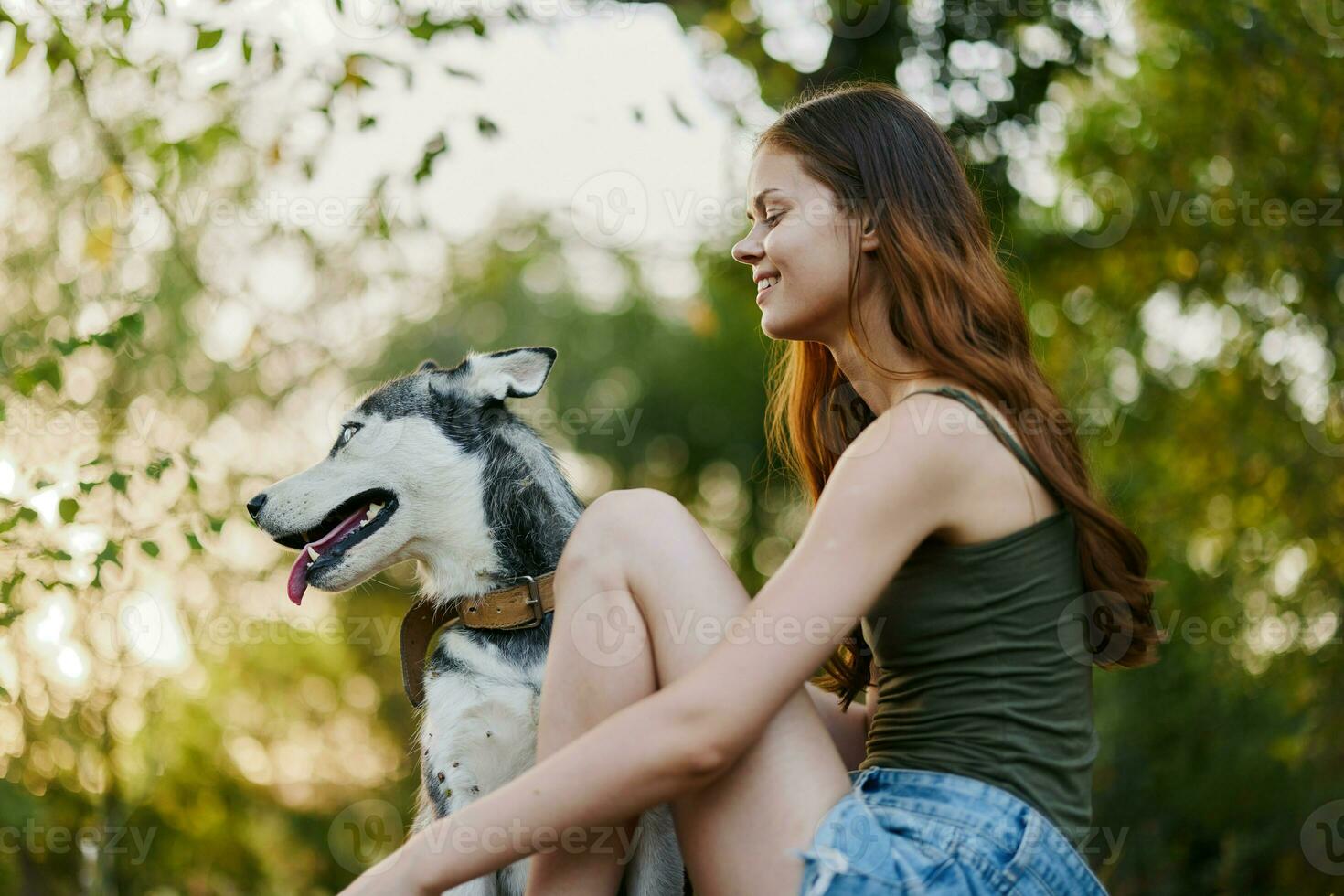 A woman with a husky breed dog smiles and affectionately strokes her beloved dog while walking in nature in the park in autumn against the backdrop of sunset photo