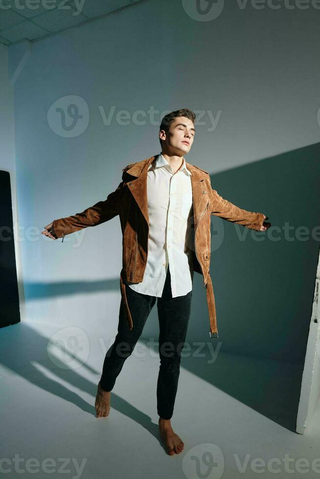 Handsome man in a brown jacket spreads his arms to the sides on a gray background top view photo