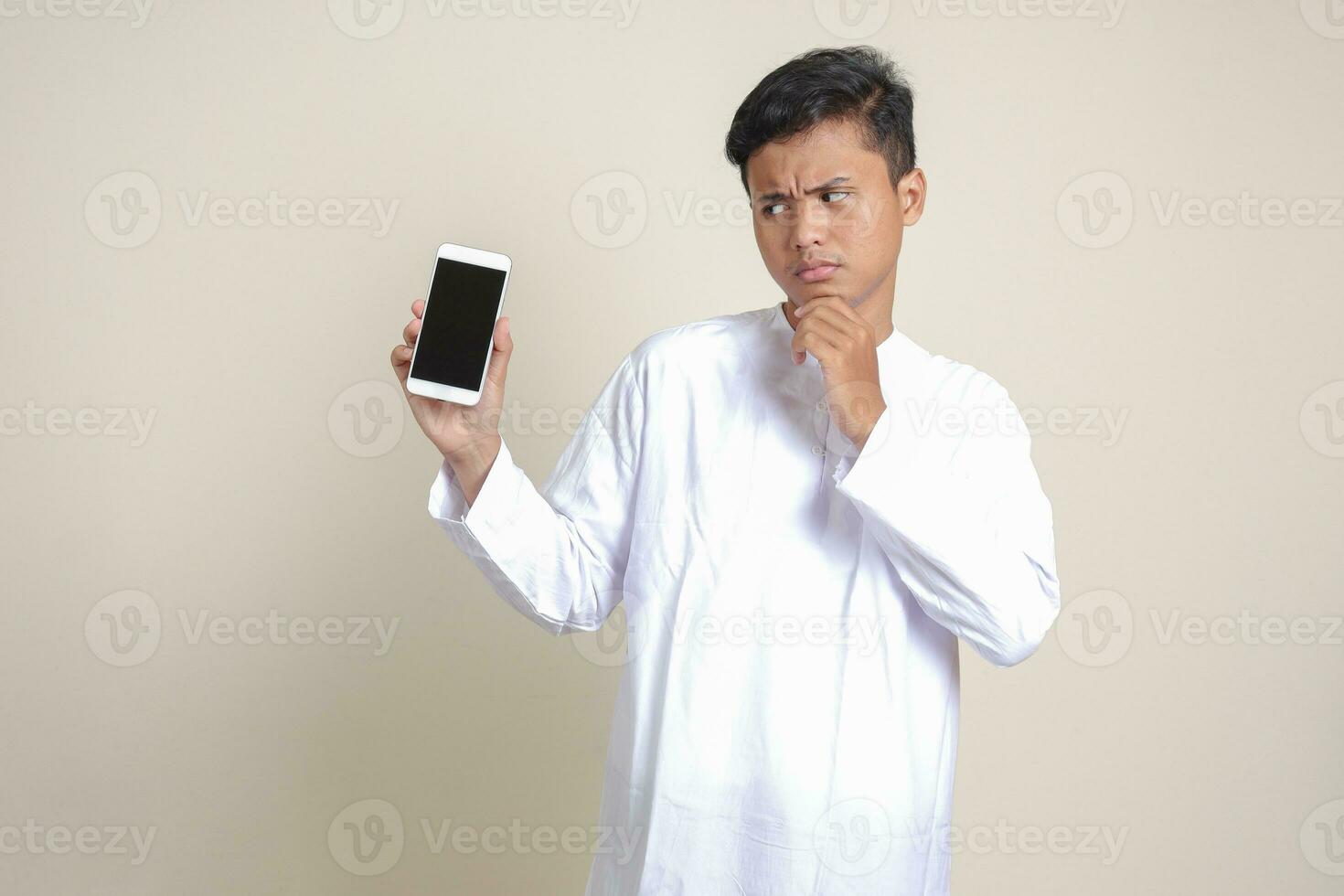 Portrait of attractive Asian muslim man in white shirt showing and presenting blank screen mobile phone. Advertising concept. Isolated image on gray photo
