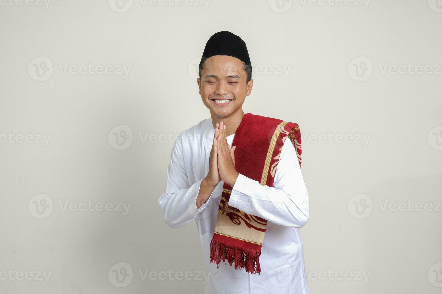Portrait of attractive Asian muslim man in white shirt with skullcap showing apologize and welcome hand gesture. Isolated image on gray background photo