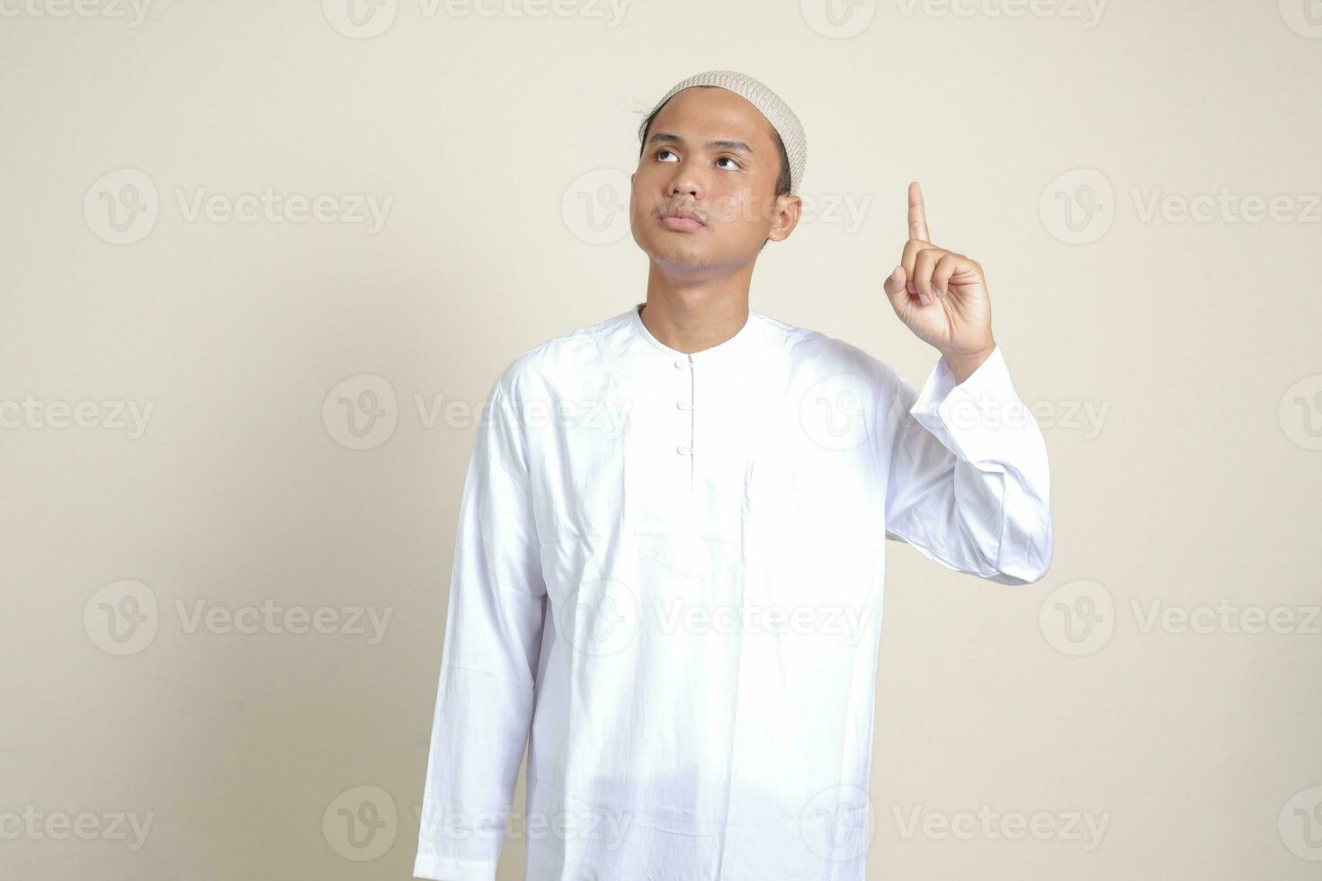 Portrait of attractive Asian muslim man in white shirt pointing up his forefinger and reminding something to do. Advertising concept. Isolated image on gray background photo