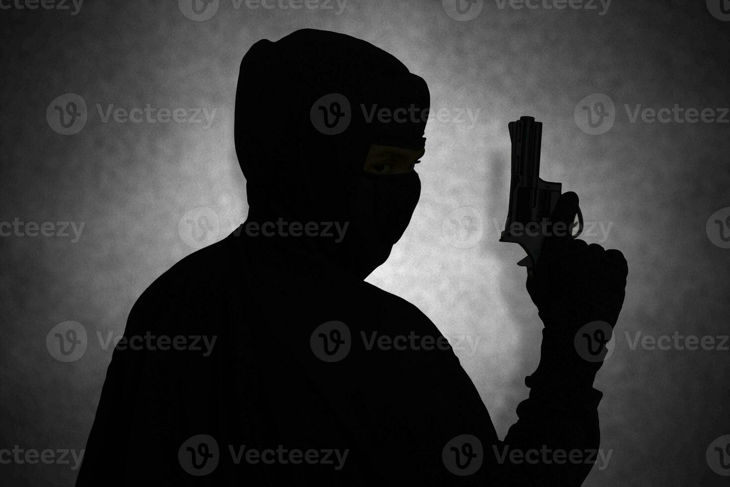 Mysterious man wearing black hoodie holding a pistol, shooting with a gun. Silhouette and dark concept image photo