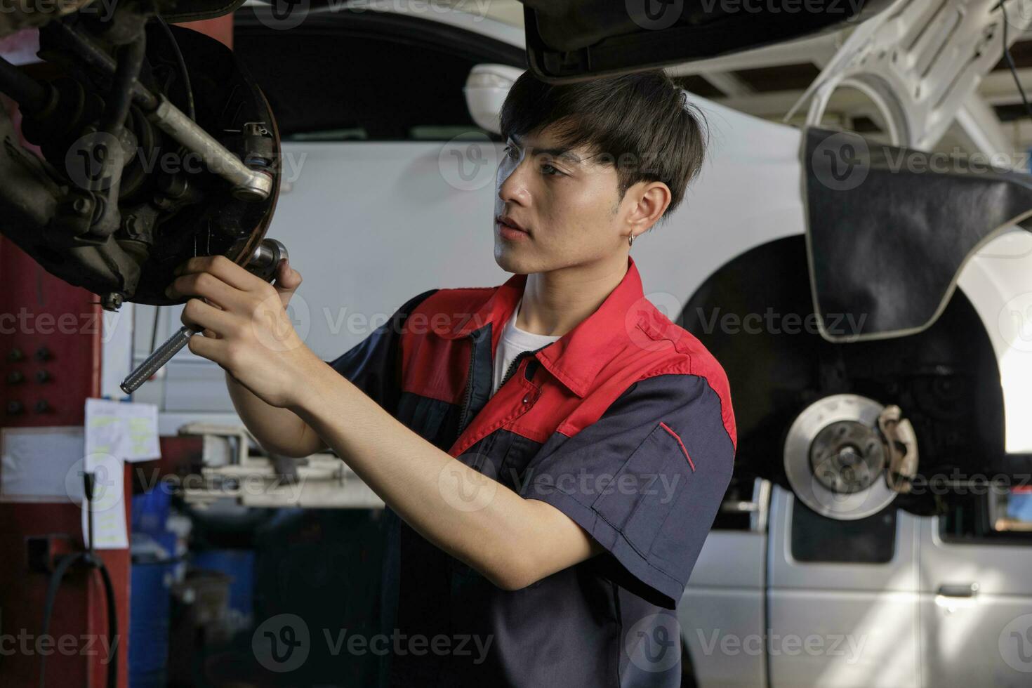 uno joven experto asiático masculino automotor mecánico técnico es atornillar coche rueda nueces en levantamiento con llave inglesa para reparar a cochera. vehículo mantenimiento Servicio obras, industria ocupación negocio trabajos. foto