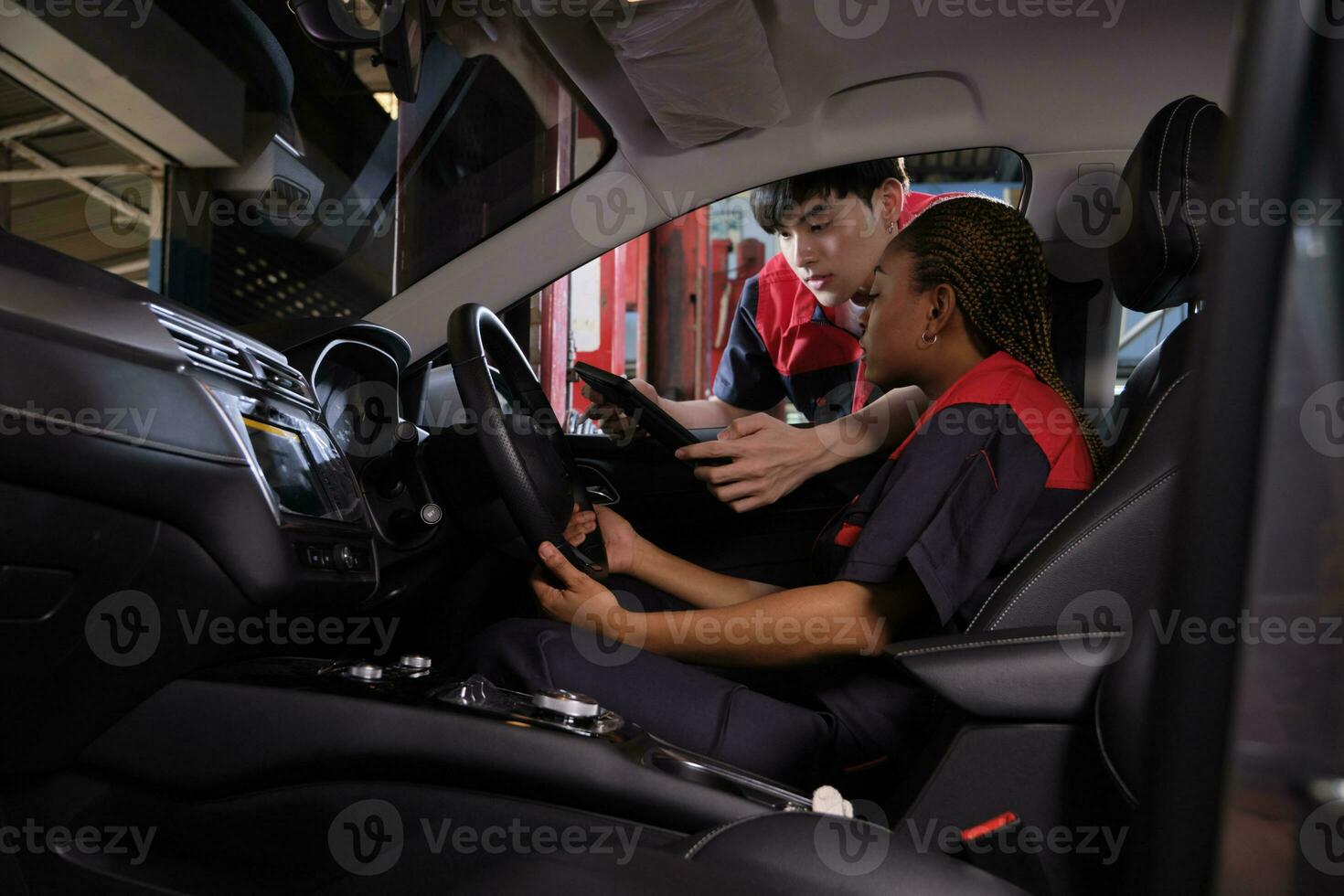 Young Black woman automotive mechanic technician and partner checking maintenance list with tablet in car interior at garage. Vehicle service fix and repair works, industrial occupation business jobs. photo