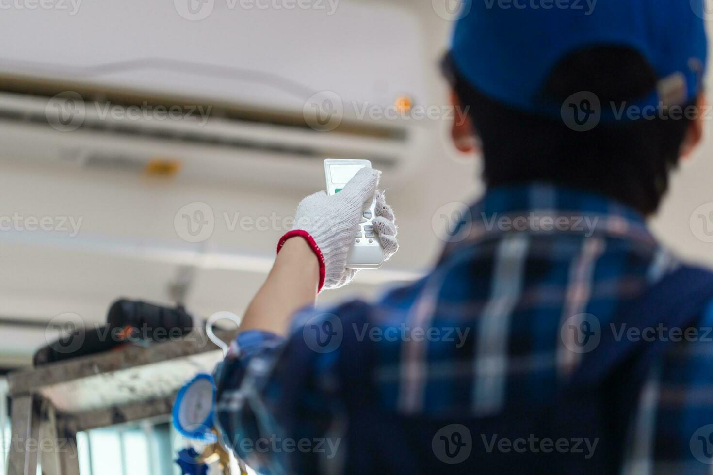 Close up of technician hand turn on air conditioner with remote control, repairman fixing air conditioner unit, Maintenance and repairing concepts photo