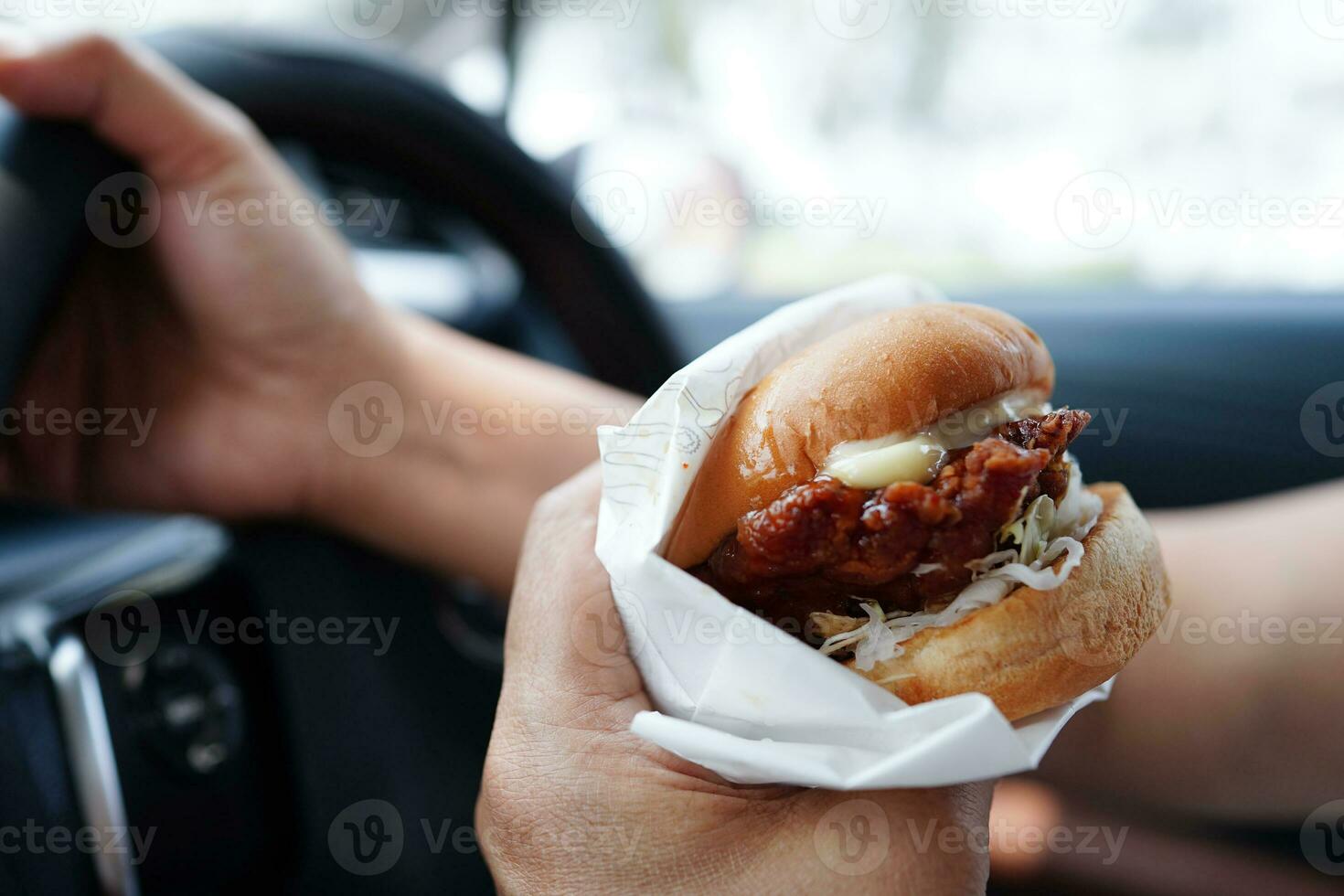 asiático mujer conductor sostener y comer hamburguesa en auto, peligroso y riesgo un accidente. foto