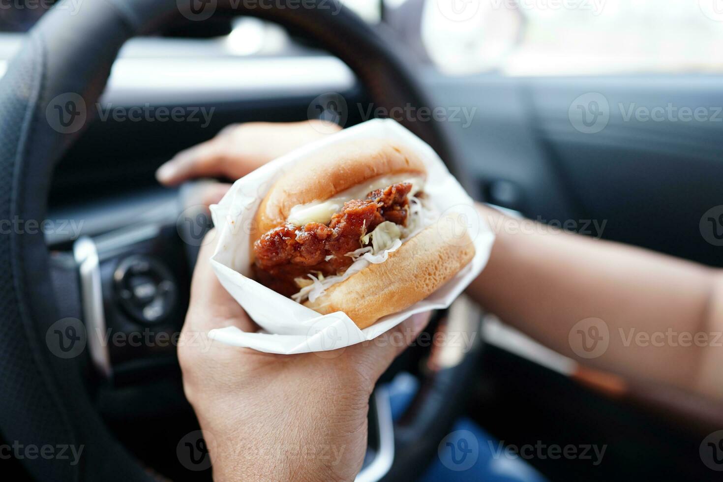 Asian woman driver hold and eat hamburger in car, dangerous and risk an accident. photo