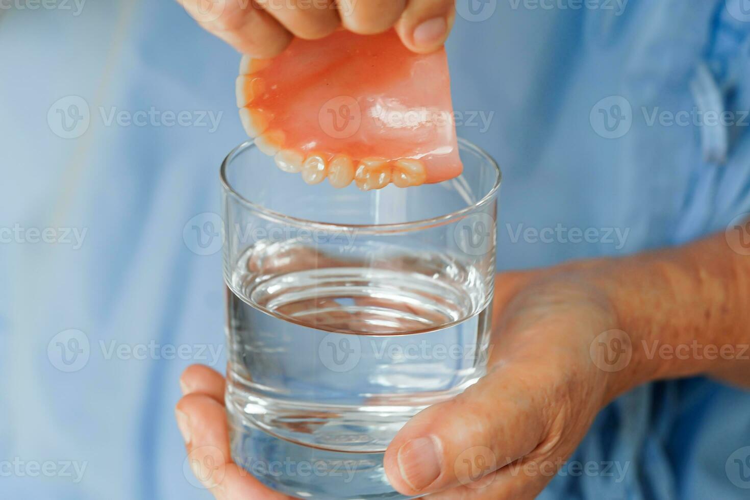 Asian senior woman patient clean teeth denture in a glass with solution for chew food. photo