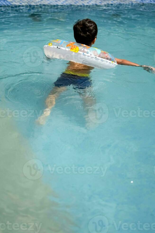 Happy Indian boy swimming in a pool, Kid wearing swimming costume along with air tube during hot summer vacations, Children boy in big swimming pool. photo