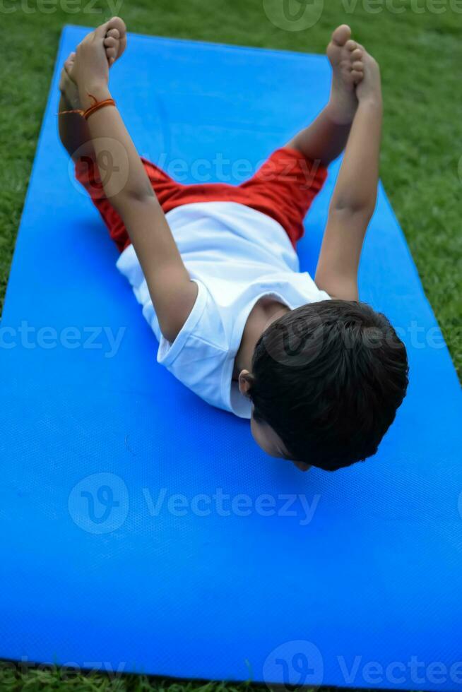 asiático inteligente niño haciendo yoga actitud en el sociedad parque exterior, para niños yoga pose. el pequeño chico haciendo yoga y meditación ejercicio. foto