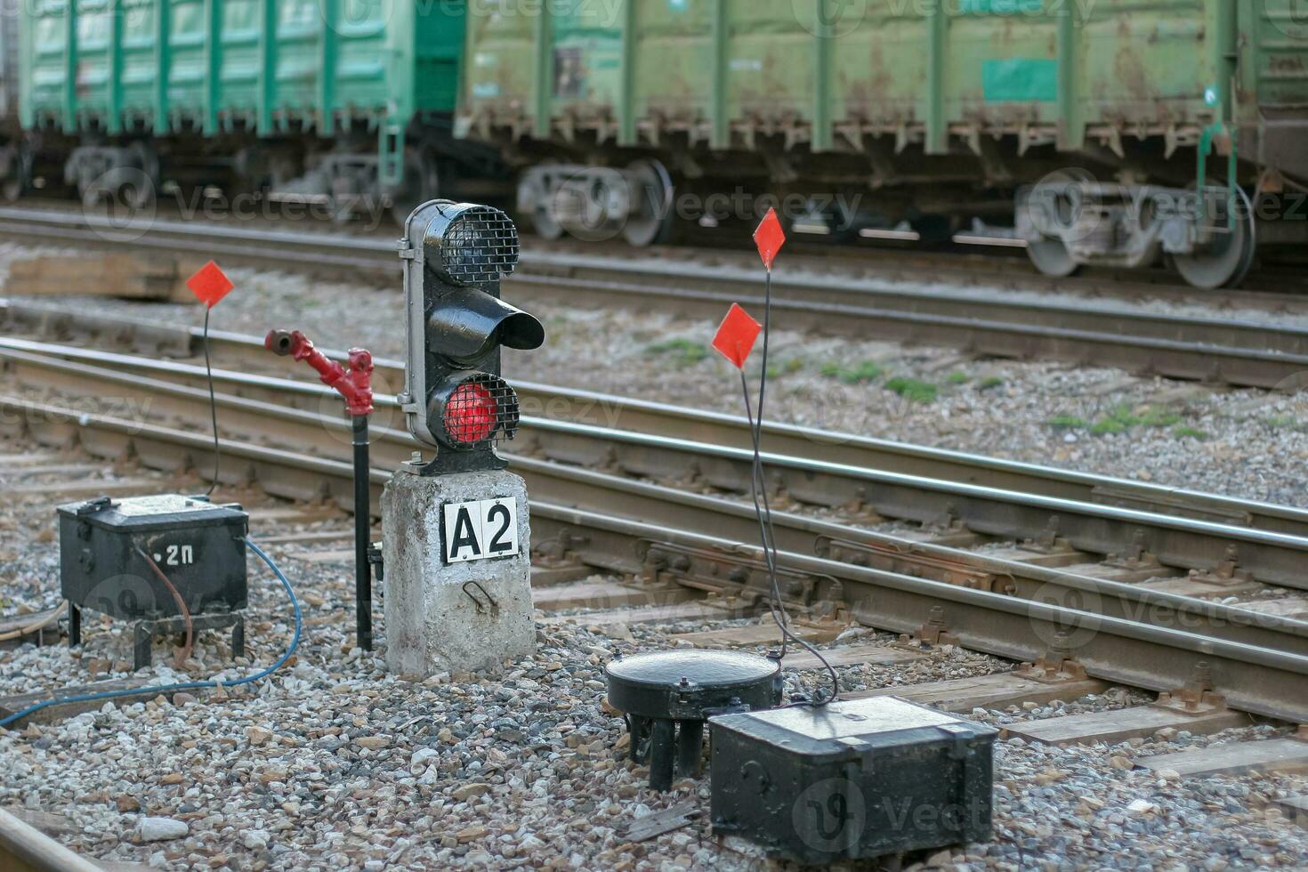 Rails with freight cars in the background and a semaphore with a glowing red light in the foreground. Selective focus on the semaphore. Background with wagons blurred. photo