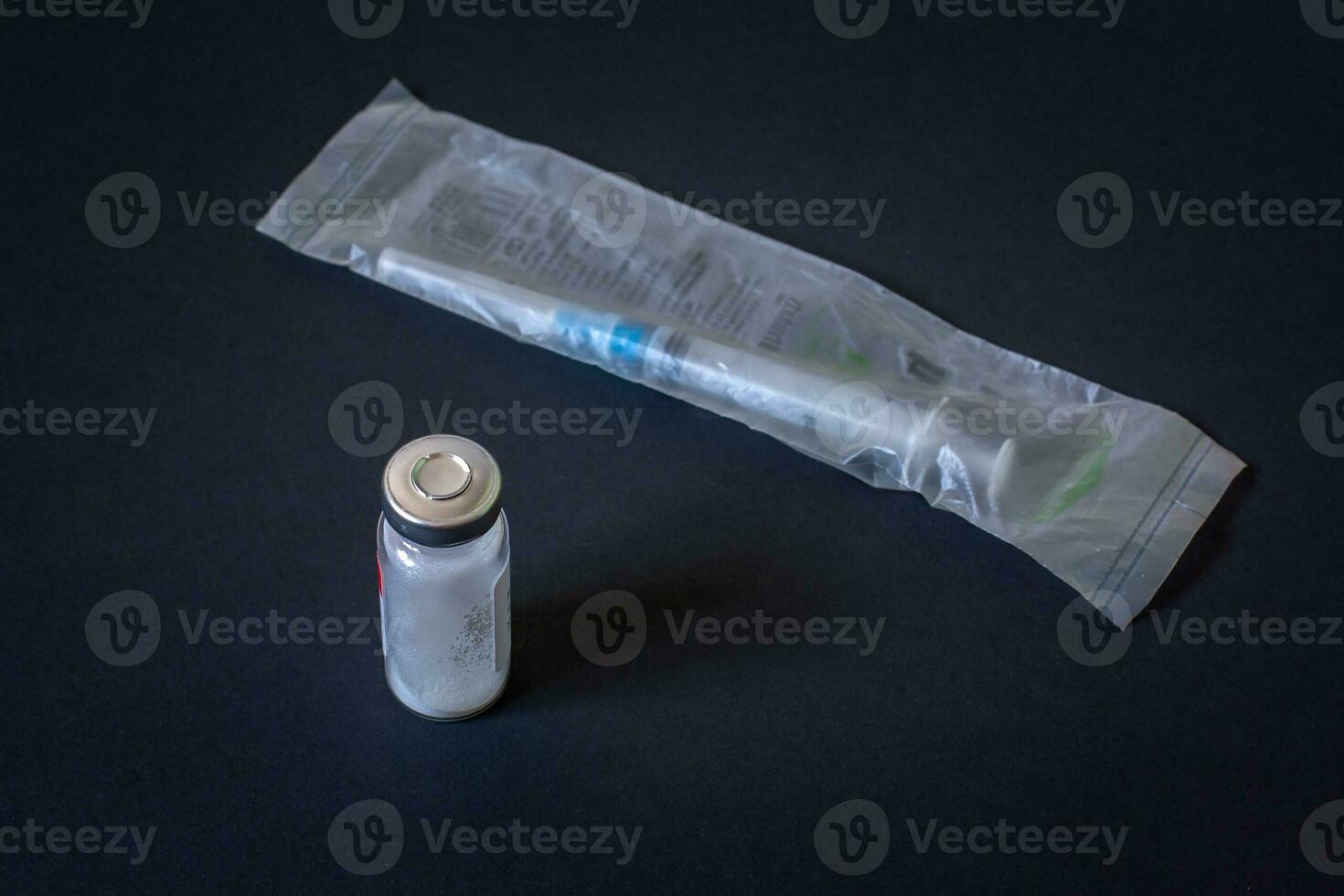 Disposable syringe in package and vial with white powder. Dark background. Horizontal. photo