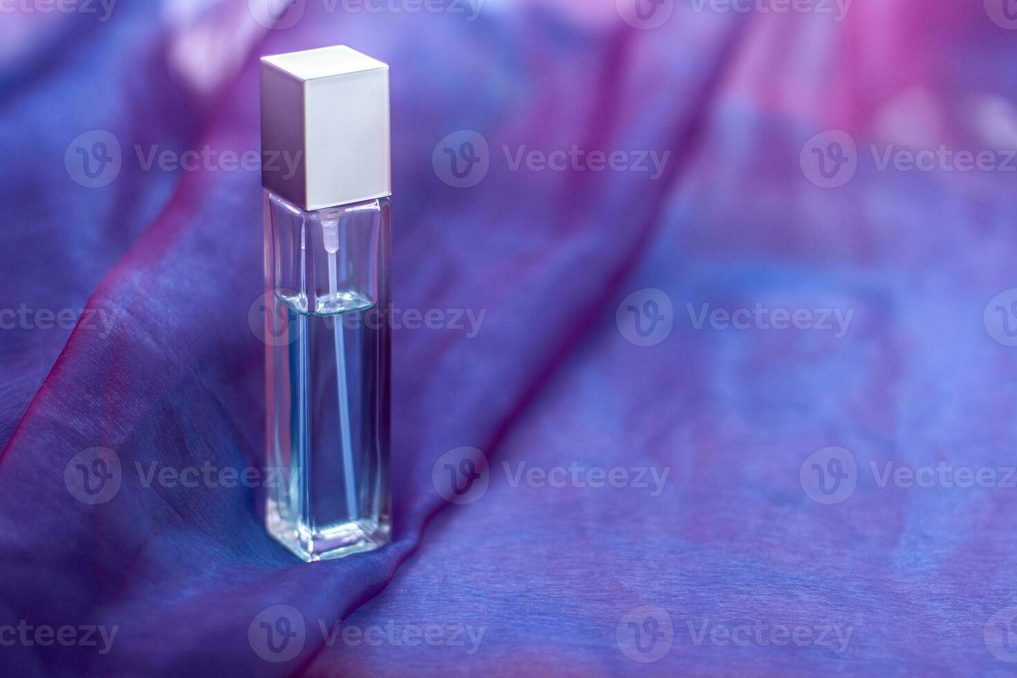 A long faceted bottle with liquid and copy space is placed on a soft cloth. An elongated glass vial with a metal cap. Blank for mock up. Shallow depth of field. Horizontal. photo