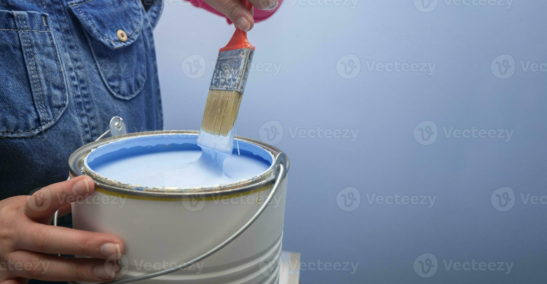 mujer vistiendo mono tomando fuera el cepillo desde el tarro de azul pintar siguiente a un azul pared foto