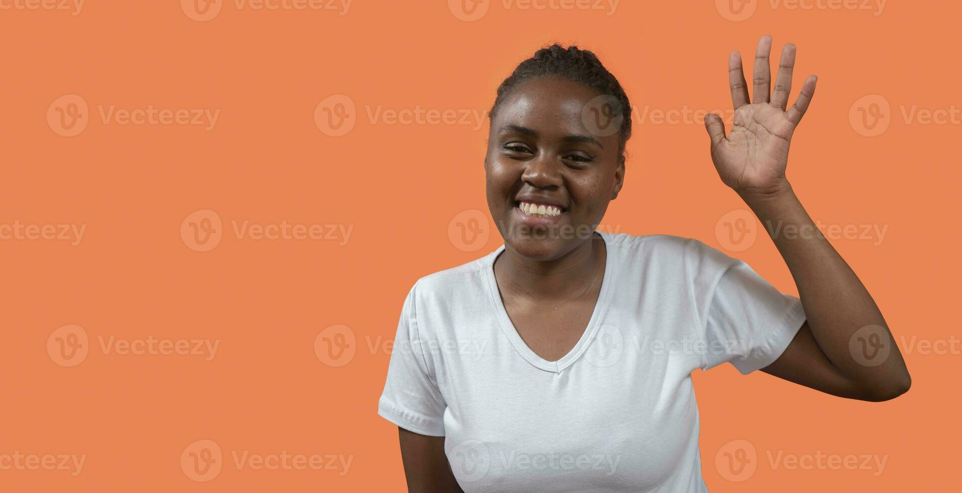 retrato de joven africano mujer mirando a cámara y ondulación mano con grande sonrisa en contra naranja antecedentes foto