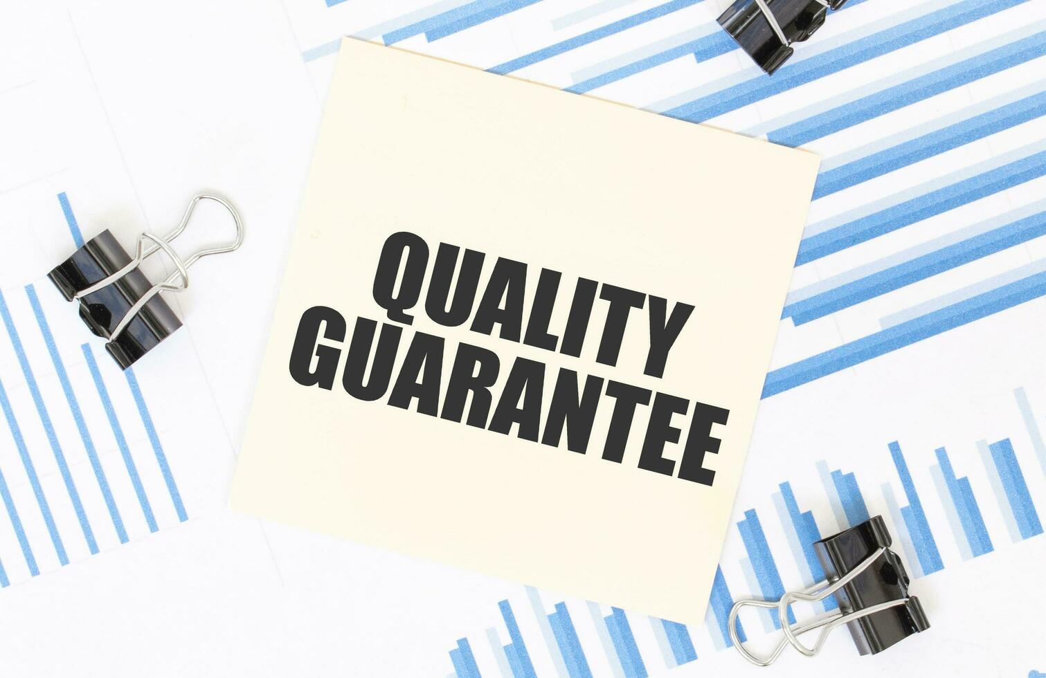 Yellow sticky notes with text quality guarantee on the white office desk. Business concept. photo