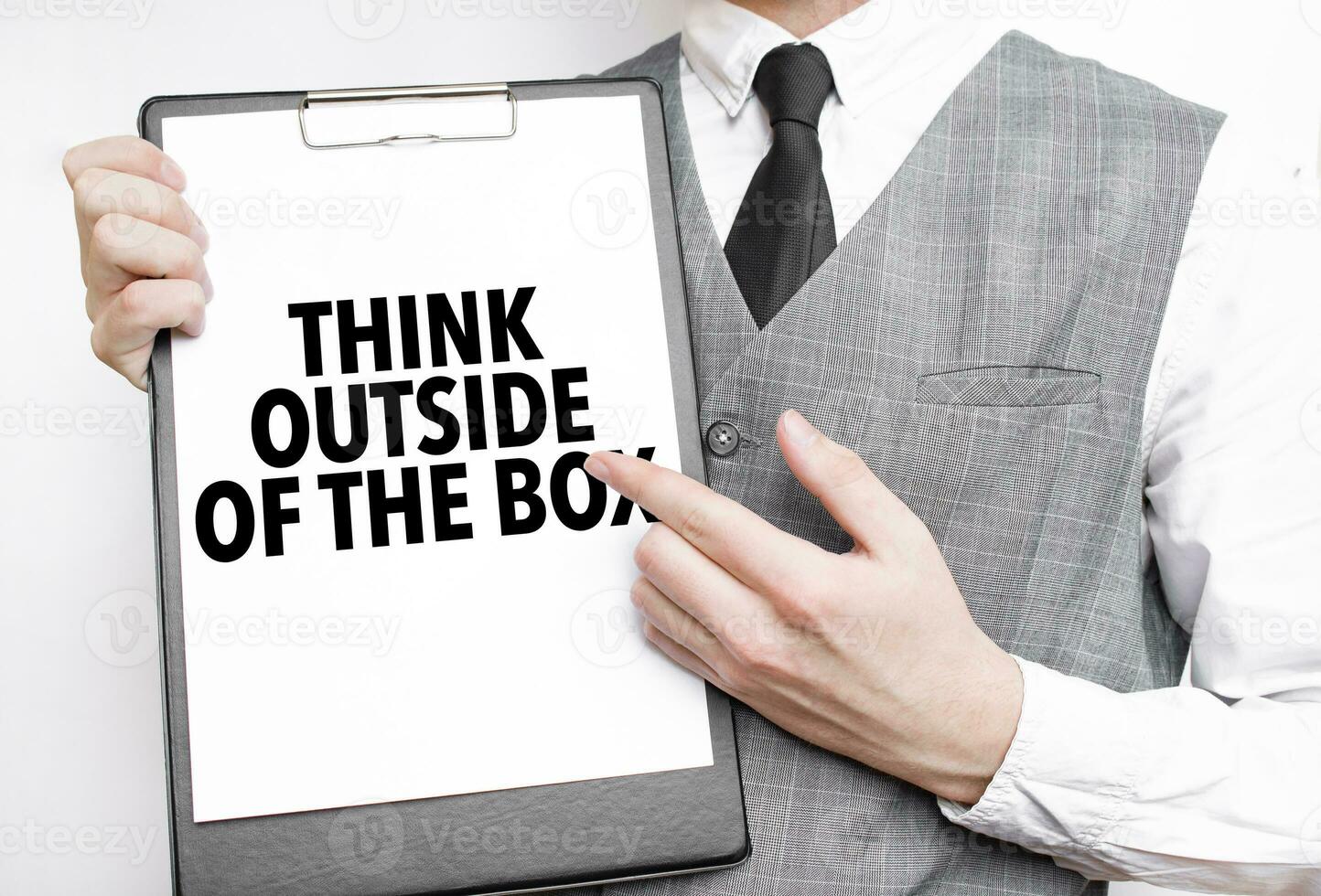 think outside of the box inscription on a notebook in the hands of a businessman on a grey background, a man points with a finger to the text photo