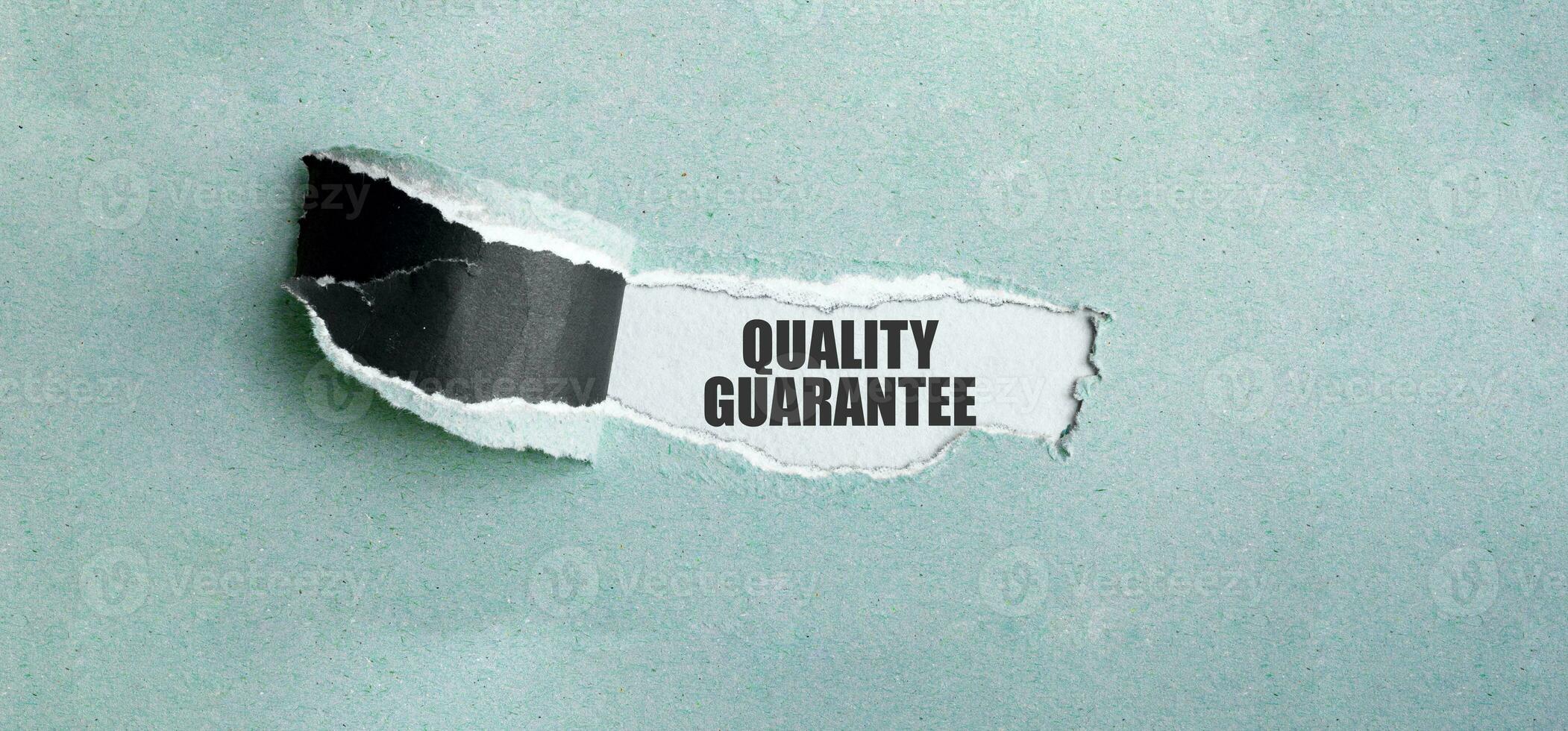 The text quality guarantee appearing behind torn green paper photo