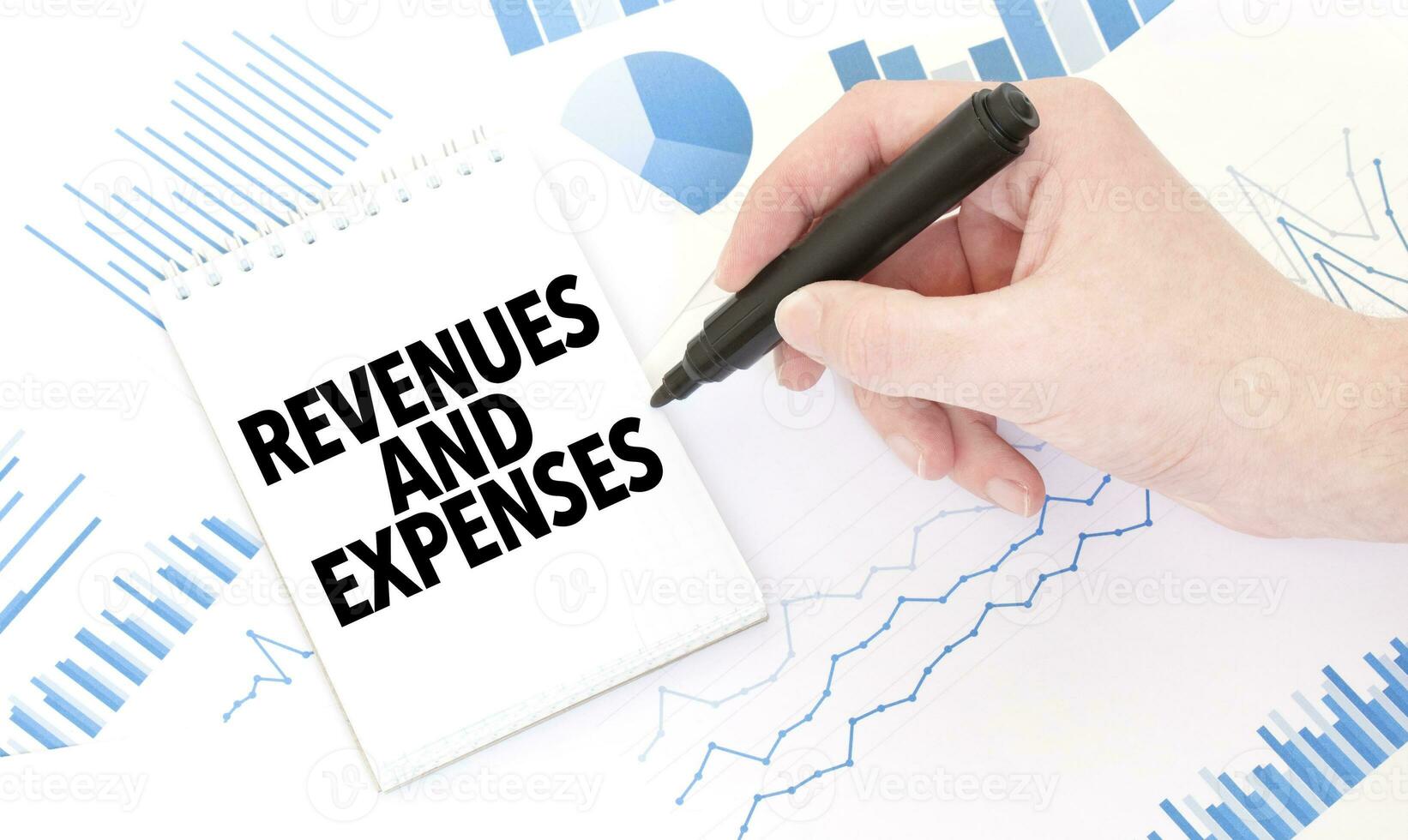 Businessman holding a black marker, notepad with text REVENUES AND EXPENSES, business concept photo