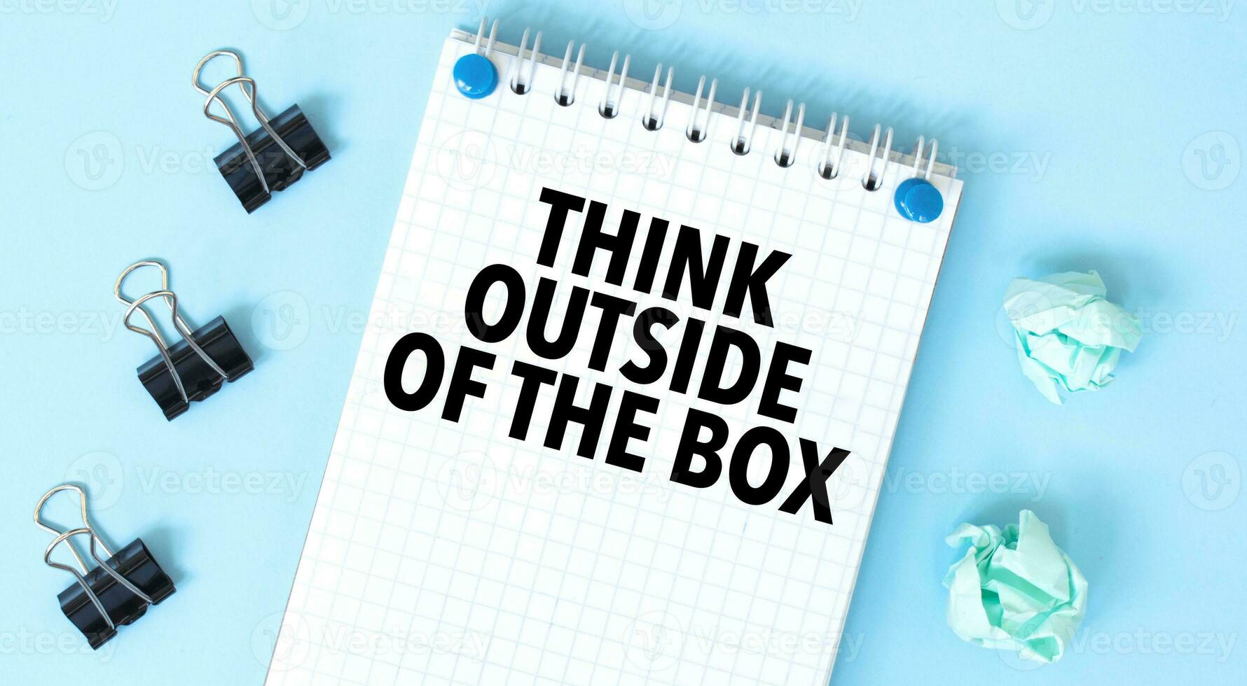 White notepad with text think outside of the box and office tools on the blue background photo