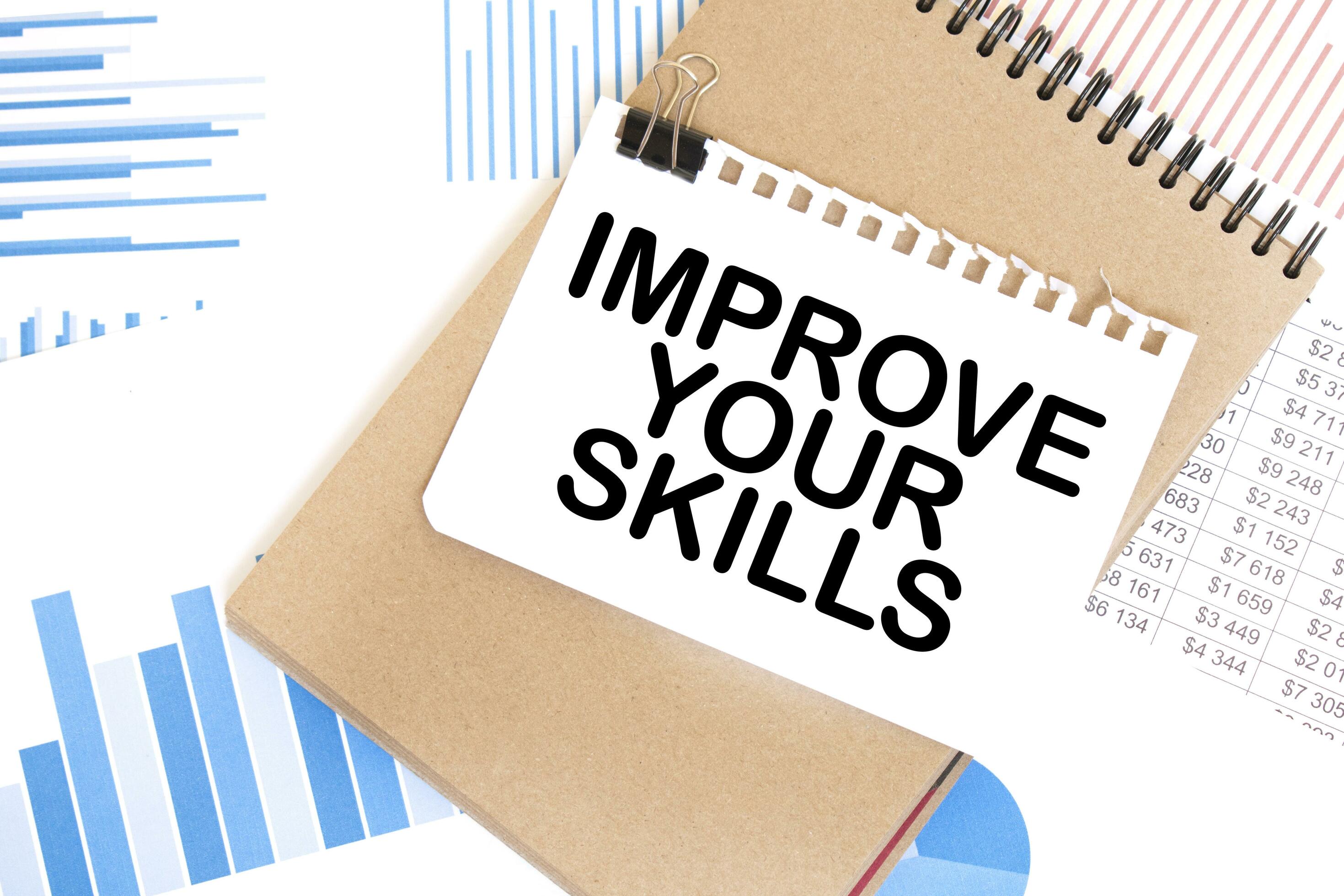 Text IMPROVE YOUR SKILLS on white paper sheet and brown paper notepad ...