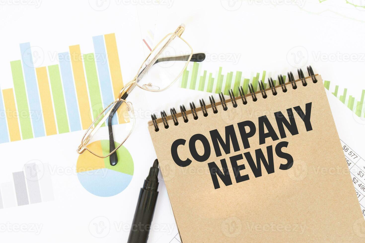 In a craft colour notebook is a COMPANY NEWS inscription, next to pencils, glasses, graphs and diagrams. photo