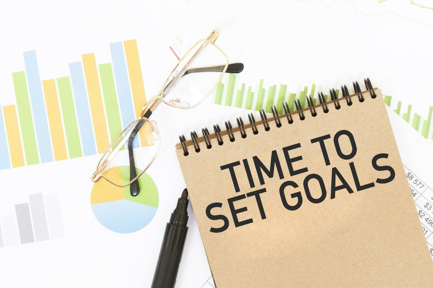 In a craft colour notebook is a TIME TO SET GOALS inscription, next to pencils, glasses, graphs and diagrams. photo