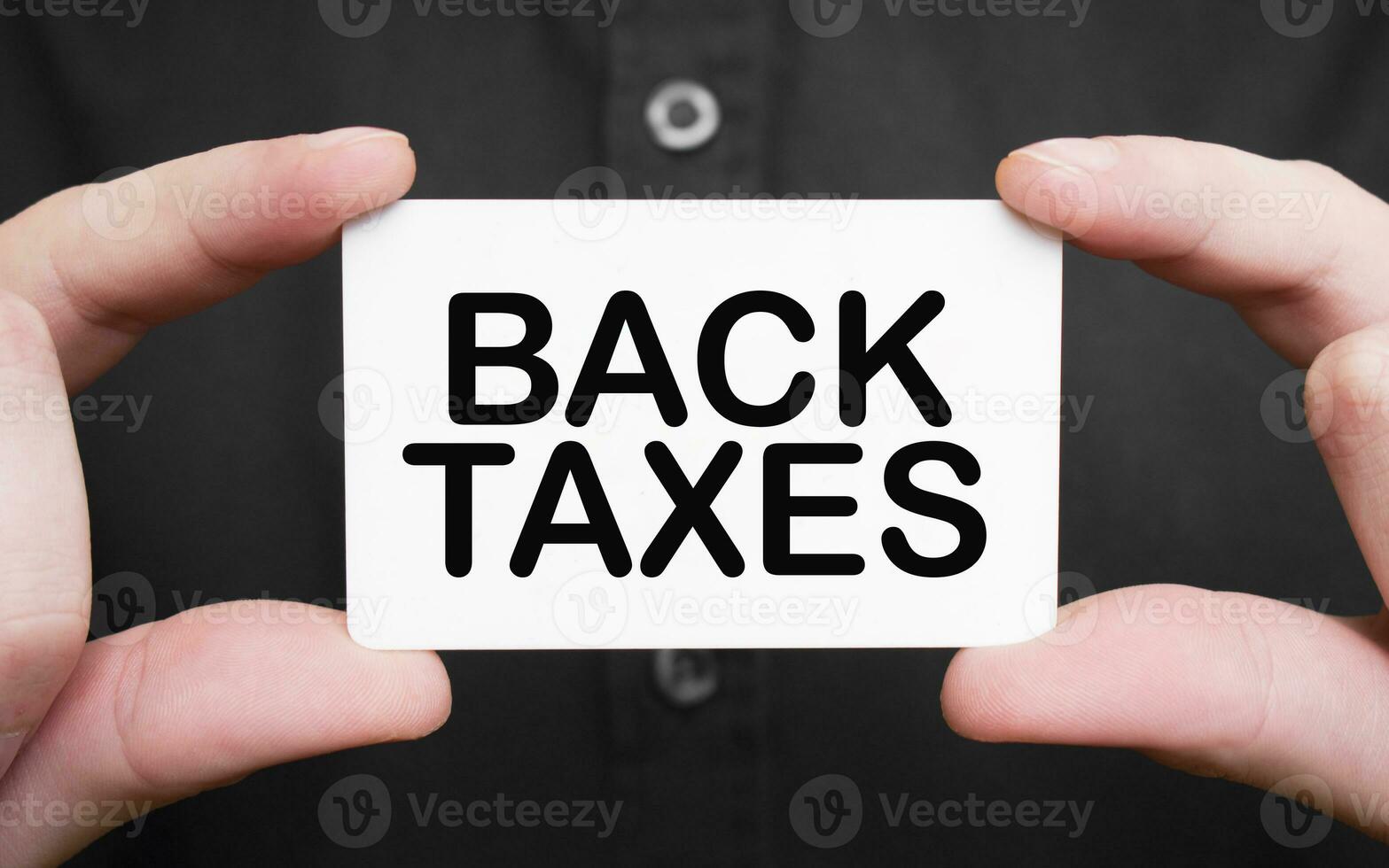 Businessman holding a card with text BACK TAXES, business concept photo