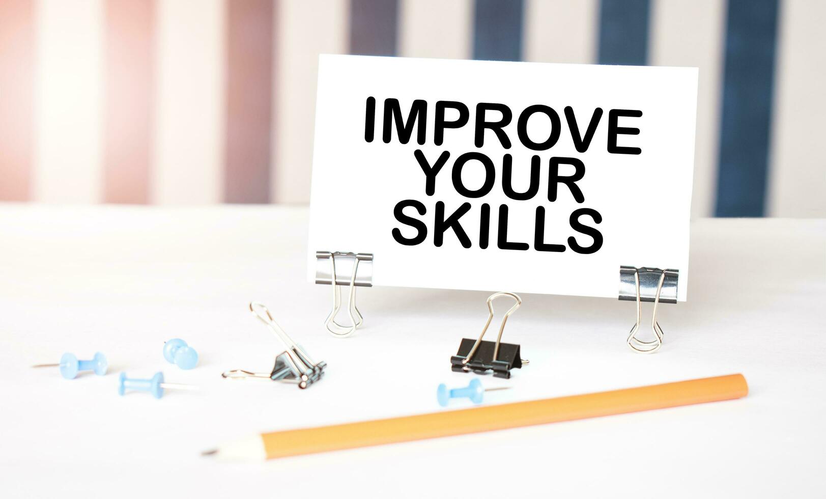 IMPROVE YOUR SKILLS sign on paper on white desk with office tools. Blue and white background photo