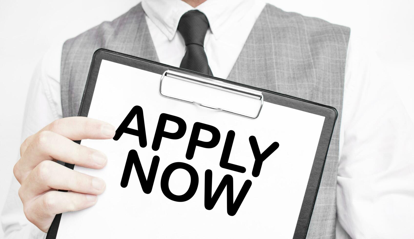 APPLY NOW inscription on a notebook in the hands of a businessman on a grey background, a man points with a finger to the text photo