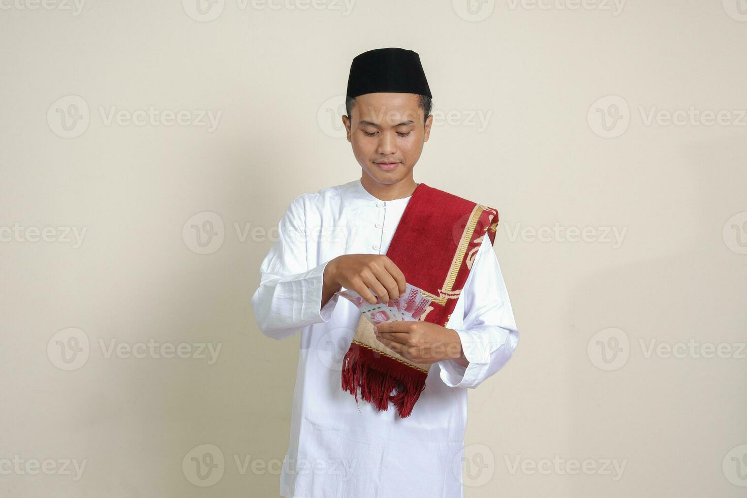 Portrait of attractive Asian muslim man in white shirt showing one hundred thousand rupiah. Financial and savings concept. Isolated image on gray background photo