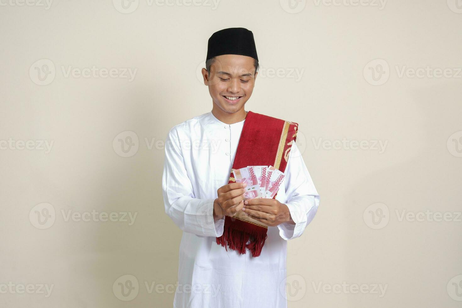 Portrait of attractive Asian muslim man in white shirt showing one hundred thousand rupiah. Financial and savings concept. Isolated image on gray background photo