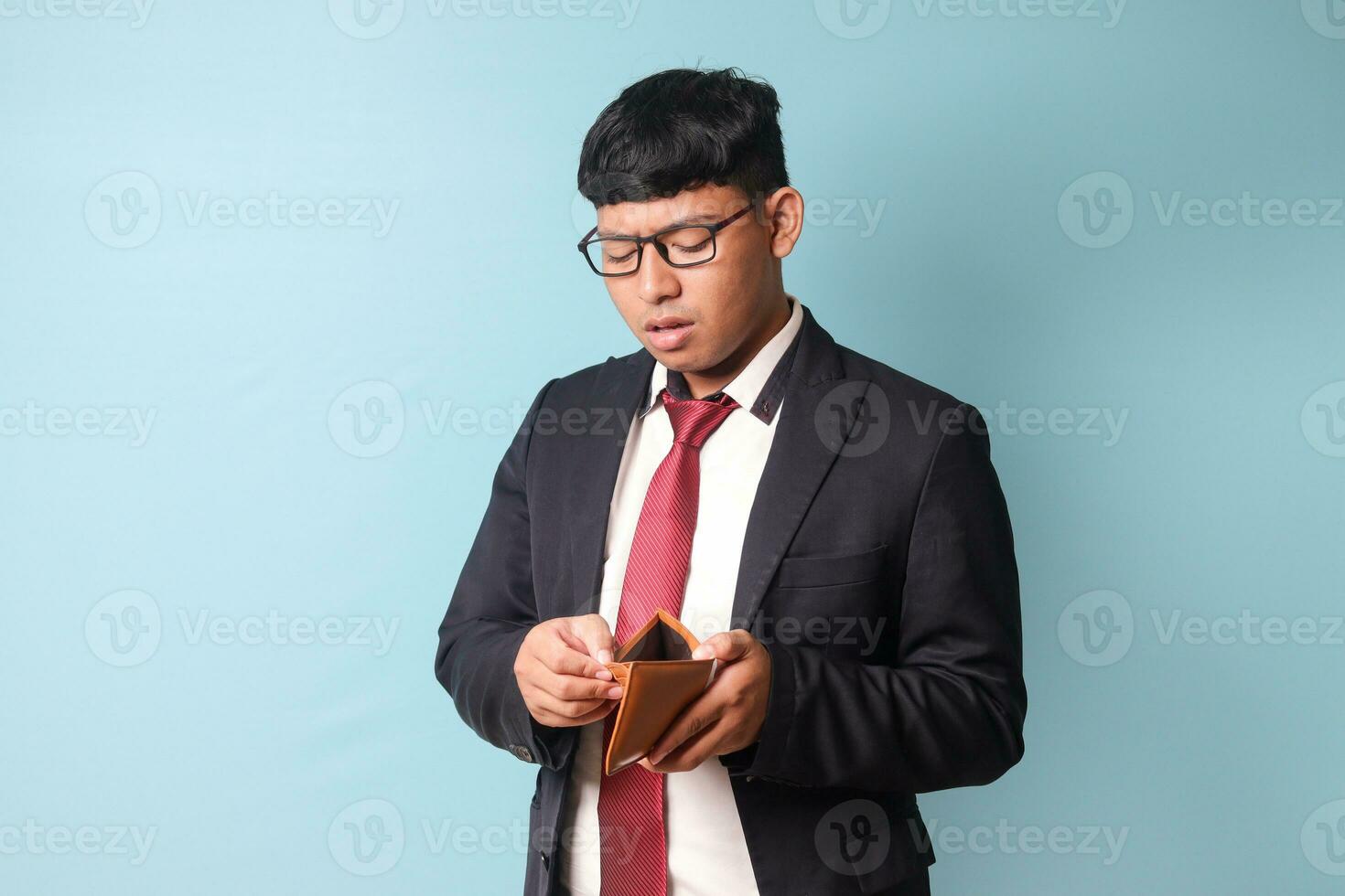 retrato de joven asiático negocio hombre en casual traje miró sorprendido mientras participación vacío cuero billetera. aislado imagen en azul antecedentes foto