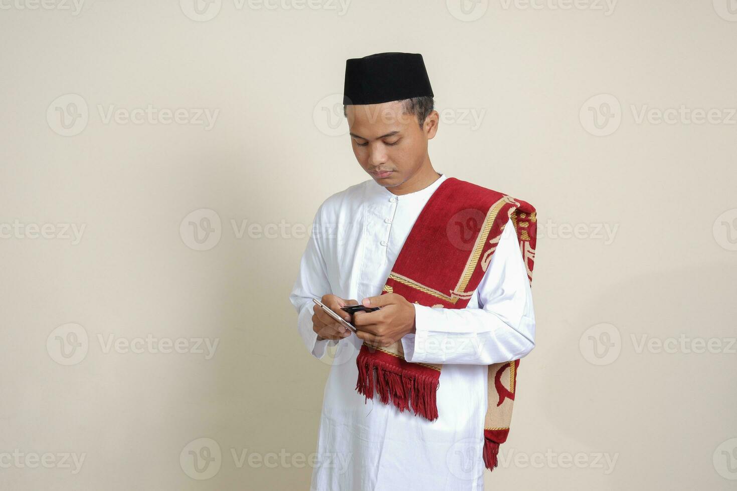 Portrait of attractive Asian muslim man in white shirt holding mobile phone with smiling expression on face. Advertising concept. Isolated image on gray photo