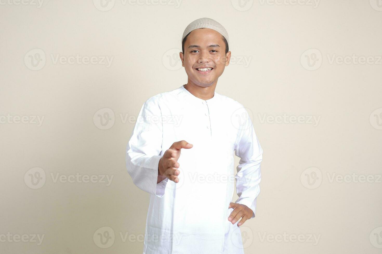 Portrait of attractive Asian muslim man in white shirt reaching out his hand for a handshake, welcoming someone. Isolated image on gray background photo