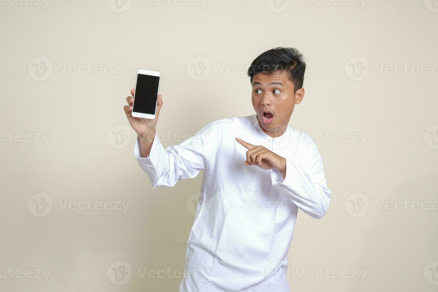 retrato de atractivo asiático musulmán hombre en blanco camisa demostración y presentación blanco pantalla móvil teléfono. publicidad concepto. aislado imagen en gris foto