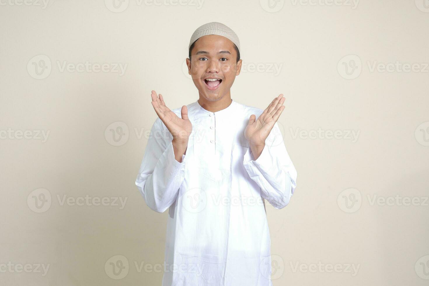 Portrait of attractive Asian muslim man in white shirt pulling hands towards camera, inviting someone to come inside, welcoming gesture. Isolated image on gray background photo