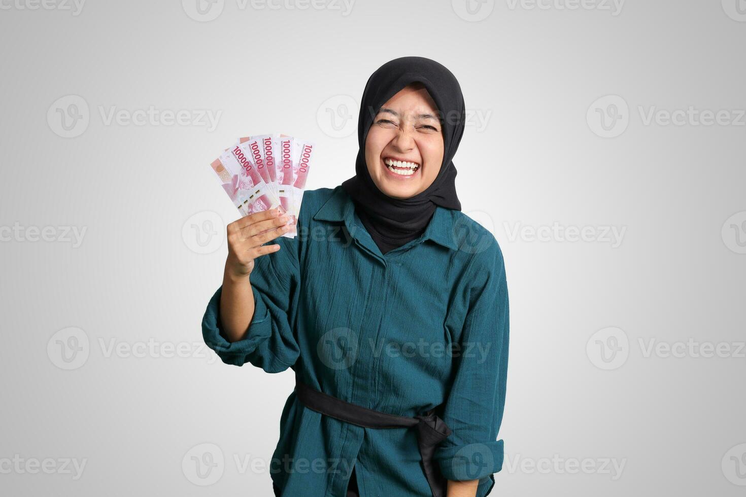 Portrait of excited Asian hijab woman in casual outfit showing one hundred thousand rupiah. Financial and savings concept. Isolated image on white background photo