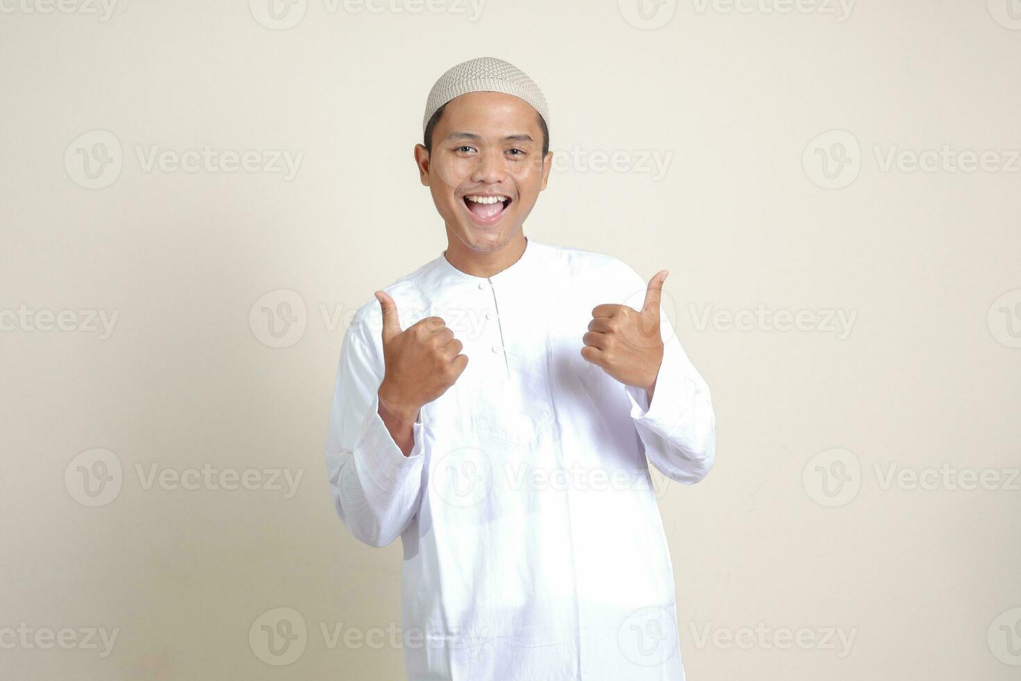 Portrait of attractive Asian muslim man in white shirt showing thumb up, good job hand gesture. Isolated image on gray background photo