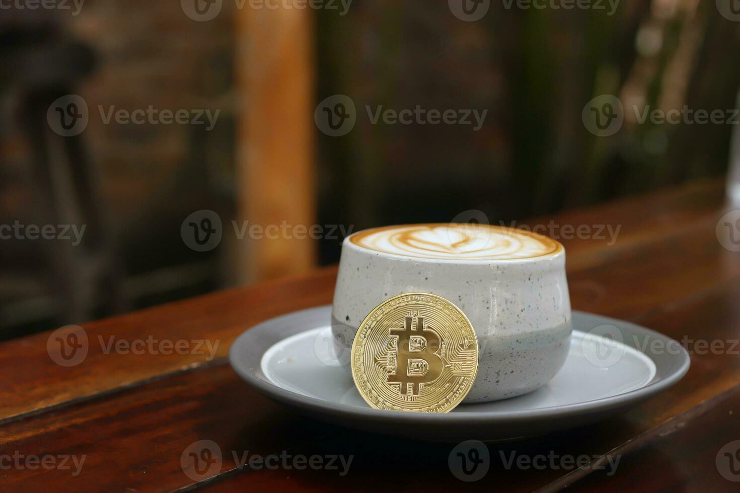 A cup of cappuccino with bitcoin on wooden table at cafe. Cryptocurrency trading concept photo