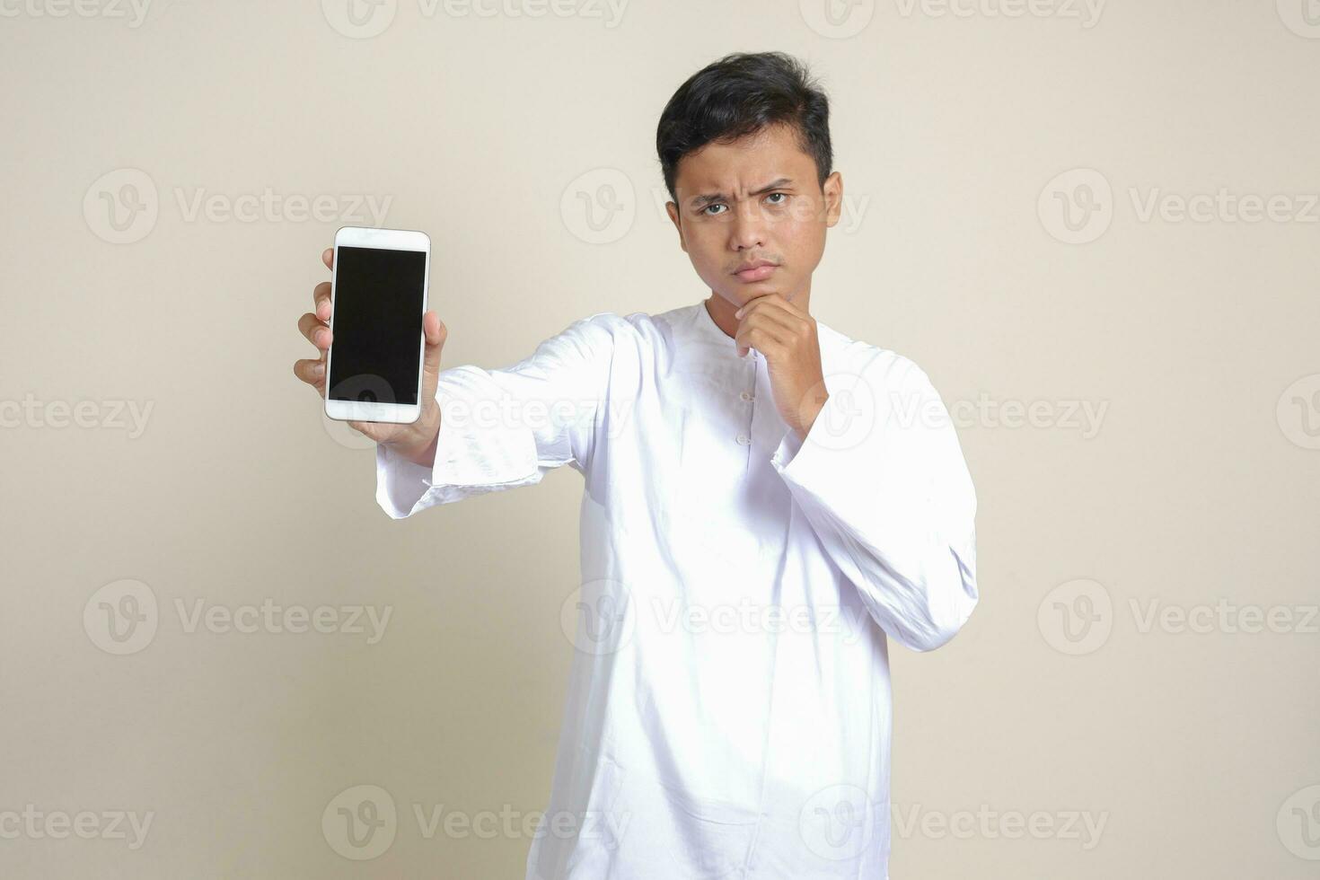 Portrait of attractive Asian muslim man in white shirt showing and presenting blank screen mobile phone. Advertising concept. Isolated image on gray photo